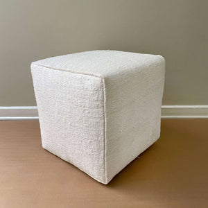 Alva Vintage Hemp Pouf on its side on a light brown floor and a beige wall - H+E Goods Company