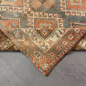 Folded edge of Atlasi Shiraz Rug on gray floor - H+E Goods Company