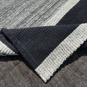 Folded edge of Meira Organic Cotton Rug on charcoal background - H+E Goods Company